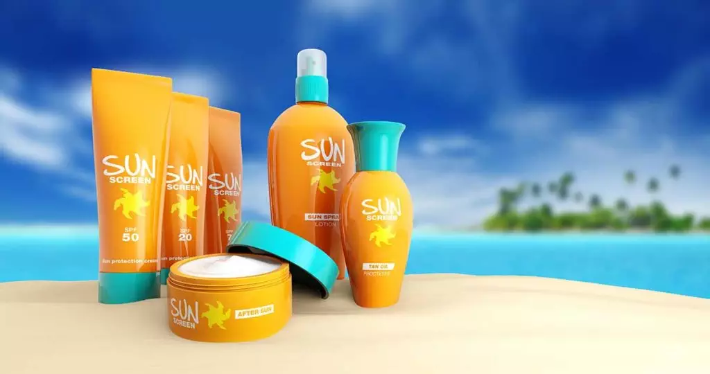 Various kinds of sunscreen containers on a beach with blue skies and water in the background
