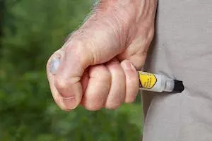 Image of man injecting an epi-pen into this thigh through his trousers