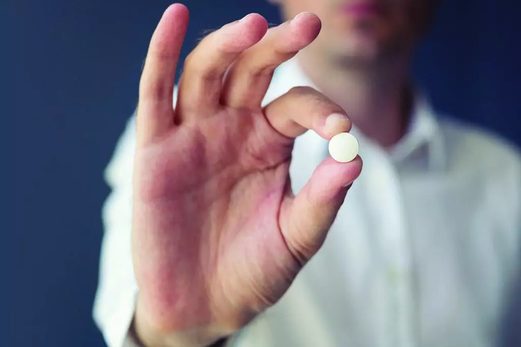 photo of man holding up an aspirin pill