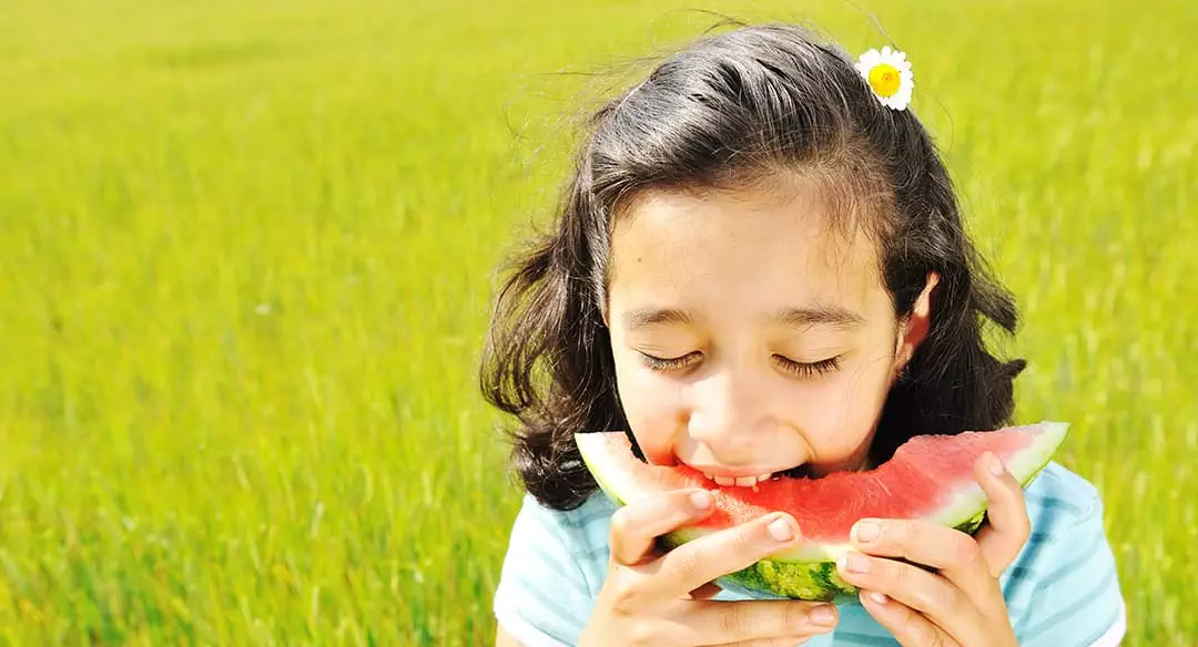 photo of young girl eating watermelon in a grassy field