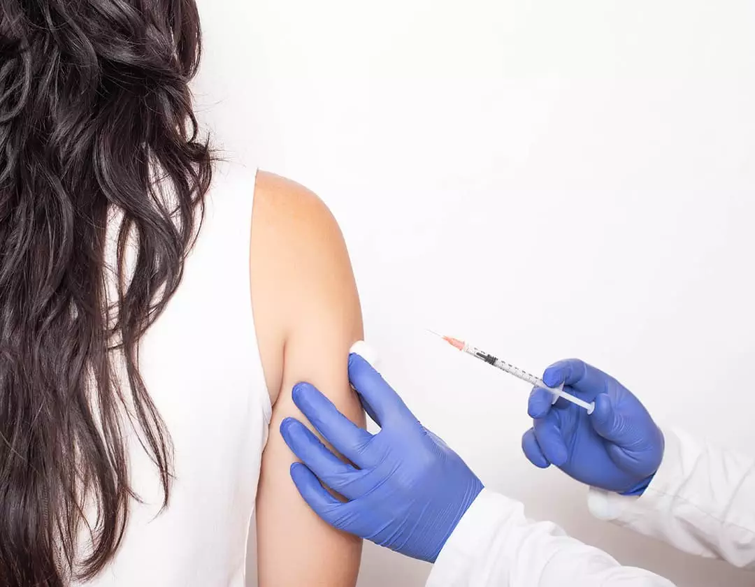 Photo of woman receiving a shot in the arm from a medical professional