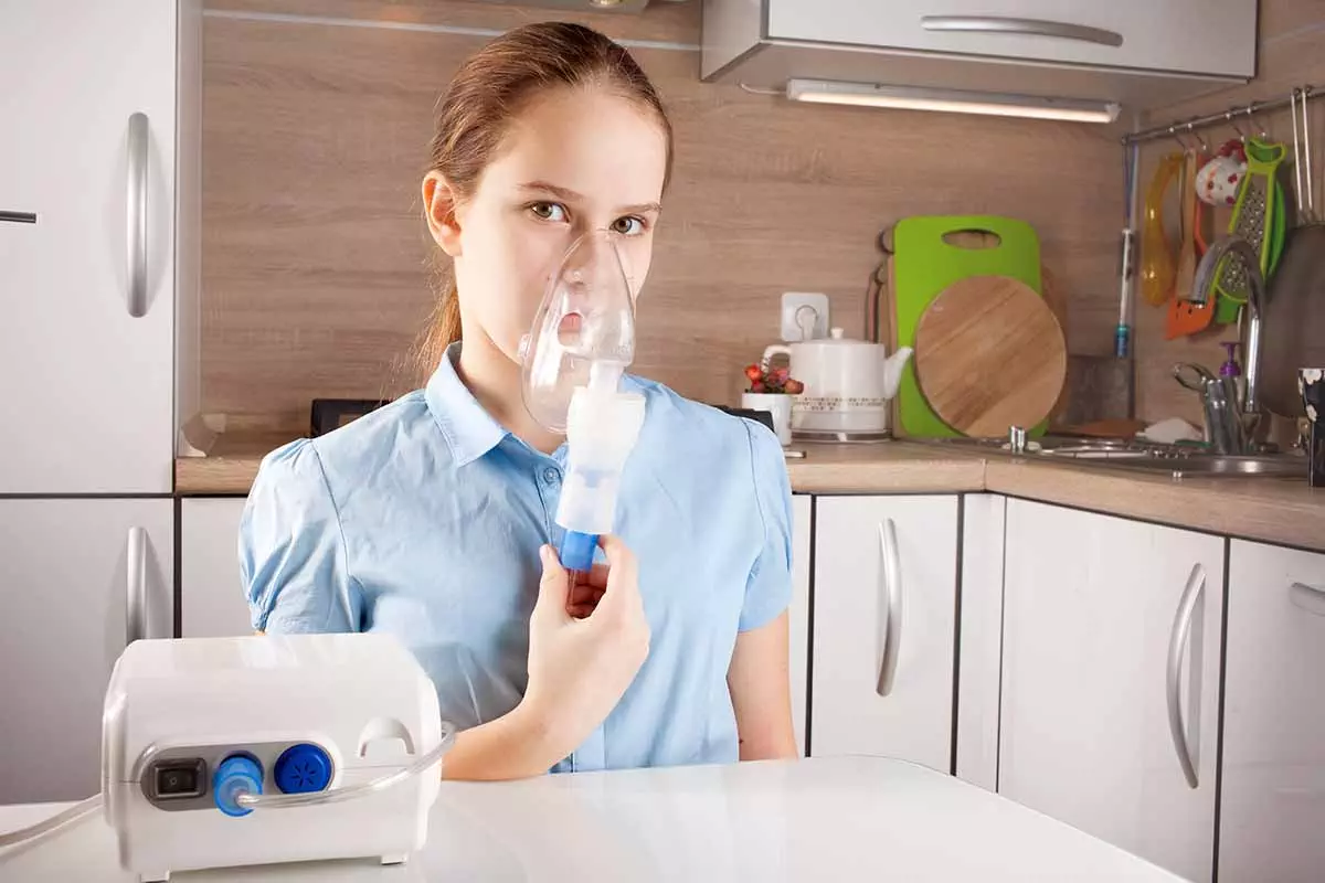 Photo of girl inhaling a nebulizer in the kitchen