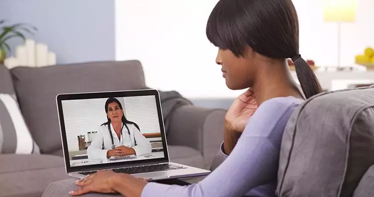 Image of woman sitting on her couch having a doctor consultation on her laptop