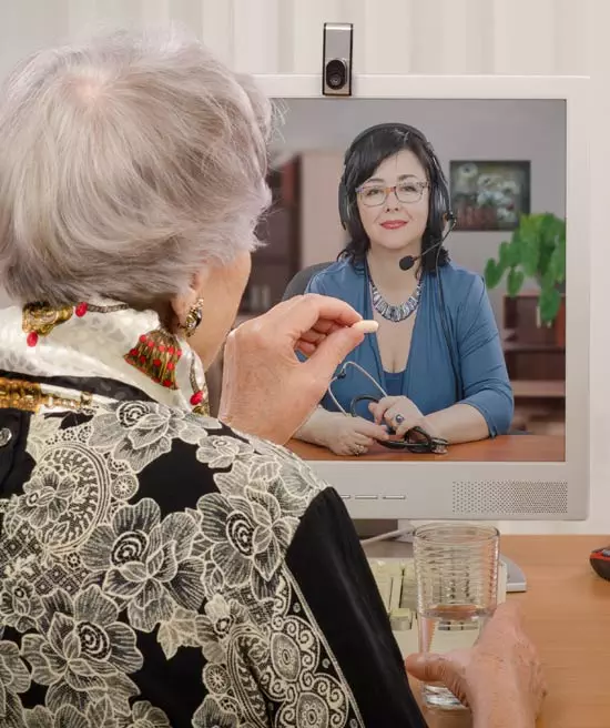 Elderly woman holding up medication to show her doctor that is online. They are in a telehealth appointment.