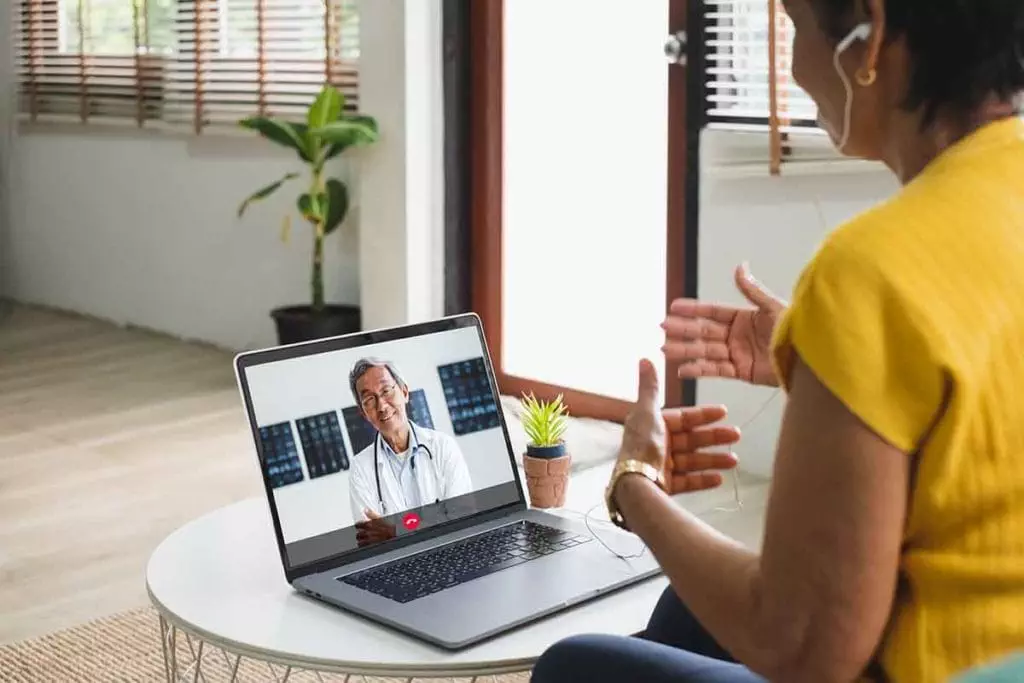 Photo of woman in her living room talking to a doctor on the computer