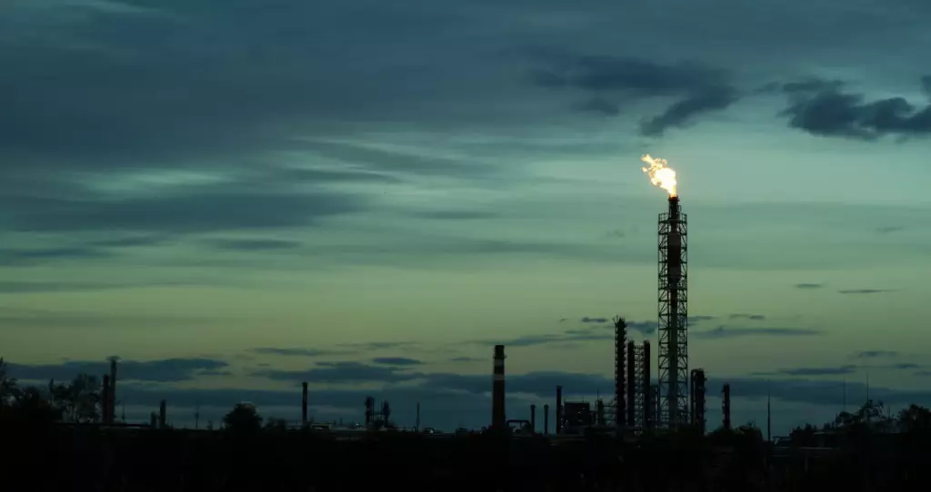 Night time photo of methane gas pollution by factories. The flame is shown coming out of one stack and the background is blueish green.