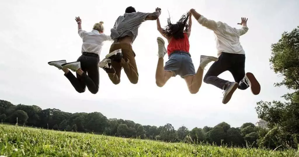 Photo of four people jumping in the air in a field