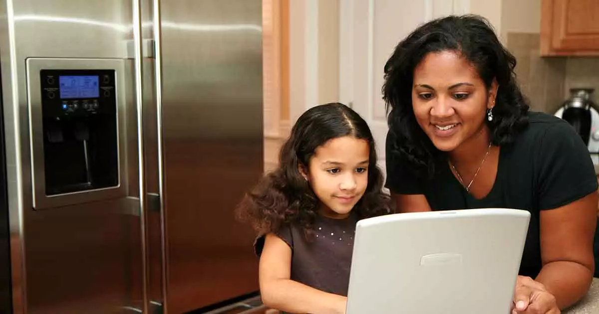 Photo of Woman in her kitchen with daughter on the computer