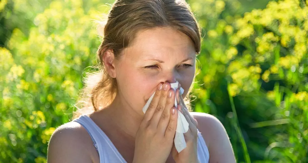 Photo of a woman suffering allergies blowing her nose in a tissue