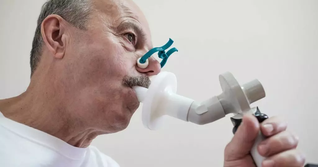 Older hispanic man using a spirometer to test for asthma at a doctor's office.