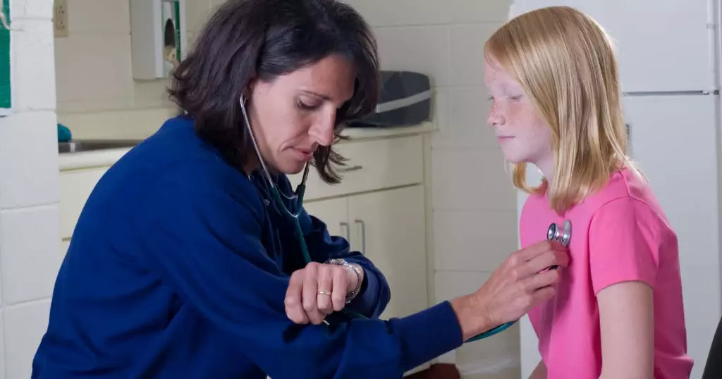 Photo of school nurse with a stethoscope checking a teen student's heart rate.
