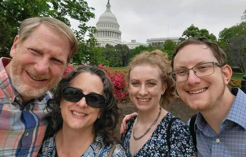 Four people from the Jensen family huddled in a photo with the US Capitol building in the background. It's a cloudy day and the family is in a garden.