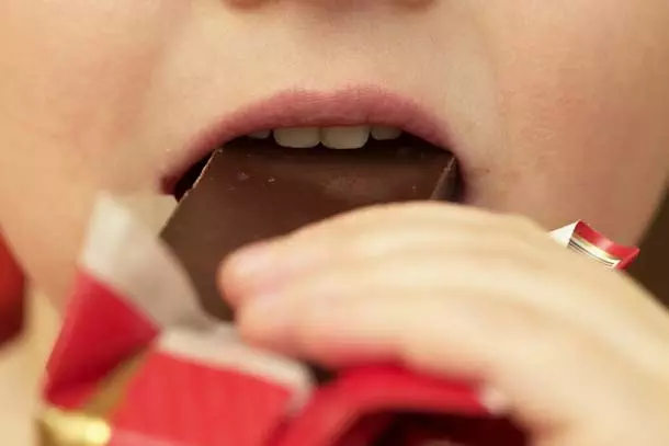 Close up of child taking a bite out of a chocolate bar