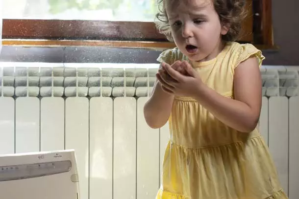 Young girl in yellow dress sneezing from the indoor air pollution in the air duct