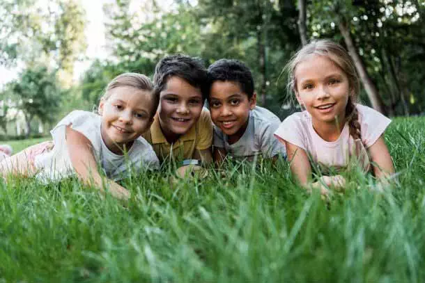 Four children laying in the grass on their bellies looking up at the camera