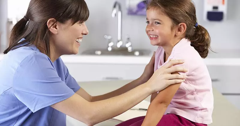 School nurse smiling with young student in nurses office at school.