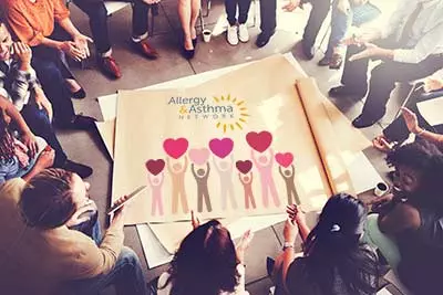 Office workers sitting in a circle looking at a poster to donate to Allergy & Asthma Network
