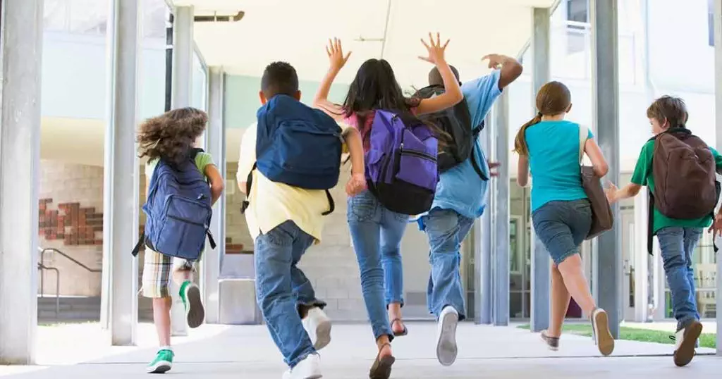 A line of children with backpacks excitedly running towards their school