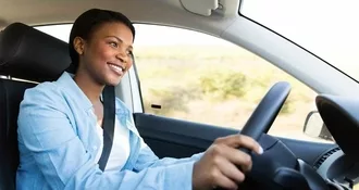 Image of woman driving a car. She is alert, aware, and is smiling.