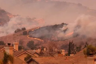 Photo of Wildfire burning on hill above houses