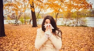 Photo of woman blowing her nose outside with fall leaves all around
