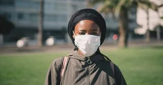 Young adult woman wearing a face mask for Covid. She's outside on a college campus and is concerned about her asthma.