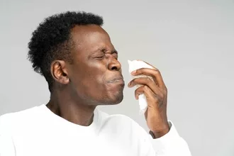 Black man ready to sneeze with a tissue near his nose.