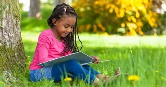 Photo of young black girl outside reading a book under a tree