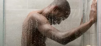PHoto of Black man taking a quick shower. His head is bent over from the pain of oncoming hives due to aquagenic urticaria