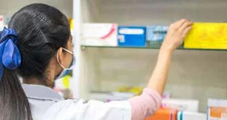 Photo of woman pharmacist taking a medicine from the shelf, wearing lab coat during work in a modern drugstore with various pharmaceutical products.