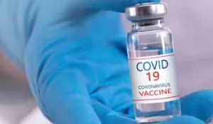 Thumbnail photo of person in surgical glove holding a vial of Covid-19 vaccine
