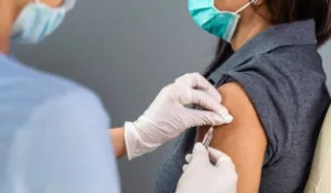 Thumbnail photo of person in surgical gloves giving woman a Covid-19 vaccine in her arm.