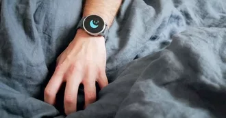 Photo of someones hand in bed wearing a watch with a moon on it