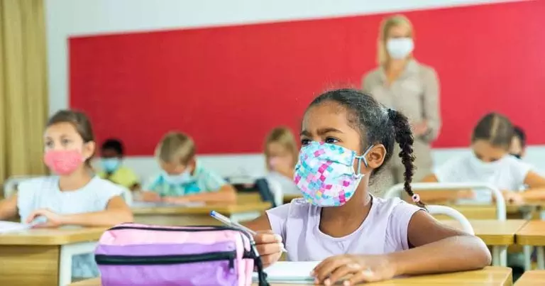 Photo of Diligent african tween girl in protective mask studying in school with classmates. New life reality in coronavirus pandemic